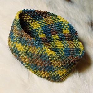K&ouml;nnte beinhalten: Ein kleiner, handgestrickter Korb in Gelb-, T&uuml;rkis- und Braunt&ouml;nen. Das Garn ist eng gewebt und erzeugt eine strukturierte Oberfl&auml;che. Das offene Design des Korbes deutet darauf hin, dass er zur Aufbewahrung oder Dekoration verwendet werden k&ouml;nnte.