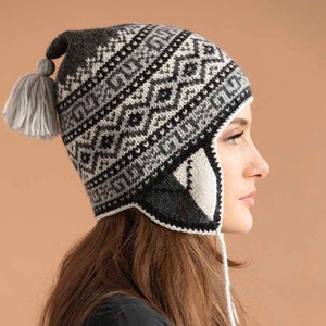 Advanced knitting pattern with some crochet for a black and white Peruvian llama chullo hat for a head circumference of 20.36 inches. It has several rows with alternating patterns, a large tassel at the crown, and earflaps with a drawstring tie.
