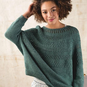 Woman in a dark green sweater knit in BC Garn Bio Balance, a soft, GOTS organic carded blend of cotton and wool. Color shown is 05 pine tree. Shop sells colors 03, 04, 05, 07, 10, 12, 14, 17, 20, 21. GOTS is the safest level of organic worldwide.