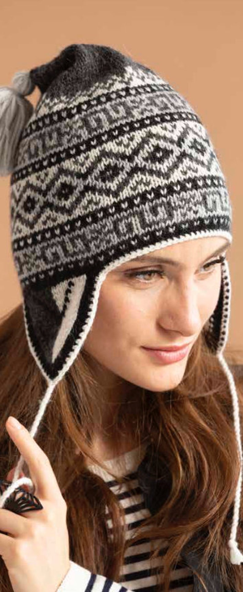 Advanced knitting pattern with some crochet for a black and white Peruvian llama chullo hat for a head circumference of 20.36 inches. It has several rows with alternating patterns, a large tassel at the crown, and earflaps with a drawstring tie.