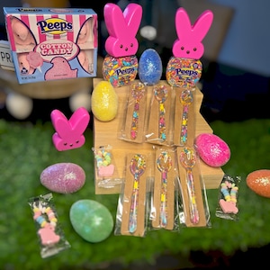 May include: A collection of Easter-themed items including a box of Peeps marshmallow cotton candy, two pink bunny-shaped containers filled with colorful sprinkles, six decorated spoons, and several glittery eggs.