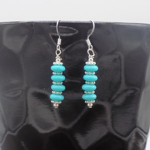 May include: A pair of dangle earrings featuring four turquoise-colored disc beads alternating with small silver-toned metal spacer beads. The earrings are suspended from silver-toned metal fishhook wires, creating a vertical, symmetrical design.