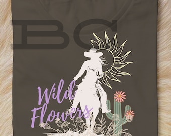May include: A brown t-shirt with a graphic design of a woman riding a horse with a cactus and flowers. The text "Wild Flowers & Wild Horses" is printed on the shirt.