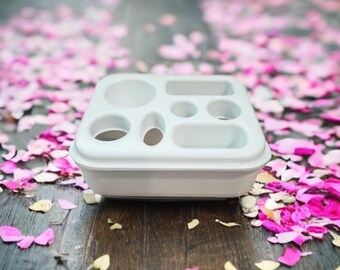 May include: White plastic organizer with multiple compartments of different sizes. The organizer is sitting on a surface covered in pink confetti.