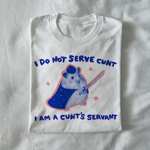 Puede incluir: Camiseta blanca con el texto "I DO NOT SERVE CUNT I AM A CUNT'S SERVANT" en azul. La camiseta presenta una ilustración azul y rosa de un hámster con capa y espada.