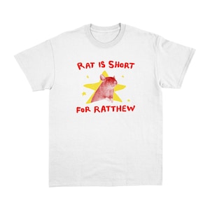 May include: White t-shirt with a graphic design featuring a red rat inside a yellow star. The text above the rat reads "RAT IS SHORT" and below it, "FOR RATTHEW" in red. The shirt is made of a soft material.