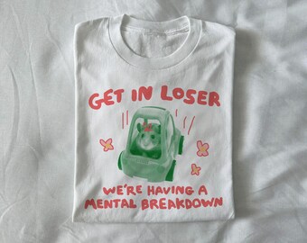 May include: White t-shirt with the text "GET IN LOSER" and "WE'RE HAVING A MENTAL BREAKDOWN" in red. A green car graphic contains a hamster with a flower crown. Pink flower graphics are also present.