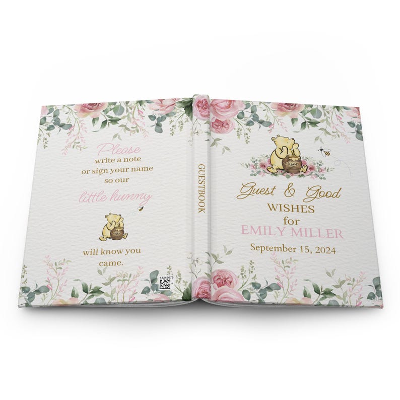 May include: A Winnie the Pooh themed guest book with a floral design. The cover features a pink floral pattern with a Winnie the Pooh illustration holding a honey pot. The text on the cover reads "Guest & Good Wishes for Emily Miller September 15, 2024".