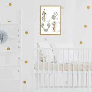 May include: A white crib with a white and beige quilted mattress and a white pillow. A framed print with the word "LOVE" spelled out with handprints and footprints is hanging on the wall behind the crib. The wall is decorated with gold polka dots.