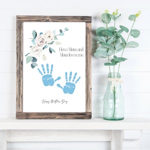 May include: A white framed print with a floral design and blue handprints. The text reads "I love Mom and Mom loves me. Happy Mother's Day."
