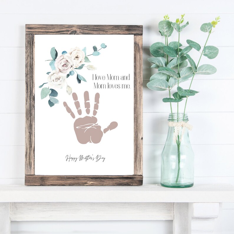 May include: A framed print with a handprint and floral design. The text reads "I love Mom and Mom loves me. Happy Mother's Day."