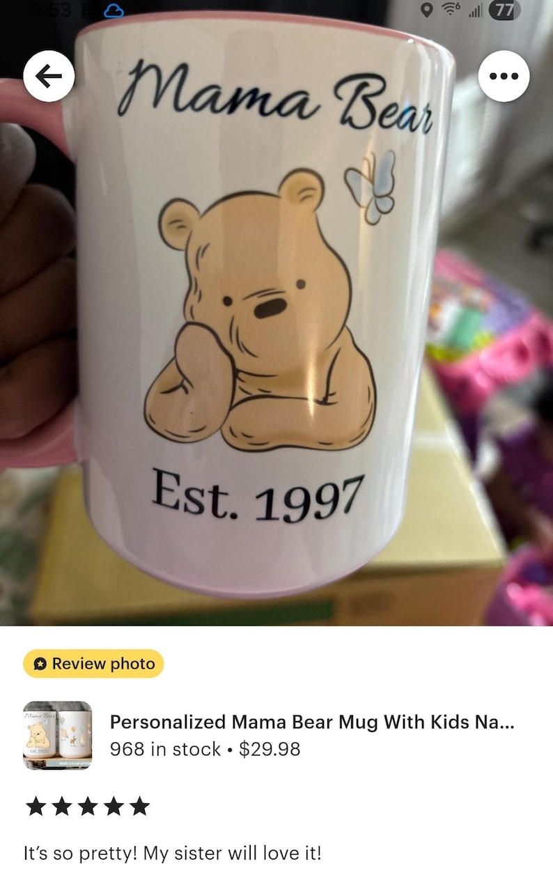 May include: White ceramic mug with a pink handle featuring a cartoon bear illustration and the words "Mama Bear" and "Est. 1997". A butterfly graphic is also present. The mug is a personalized gift.