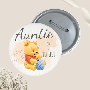 May include: Auntie-themed button with a Winnie the Pooh illustration. The button features the text "Auntie TO BEE" with a watercolor background. The design includes a cartoon bear holding a blue honey pot, with a bee flying nearby.