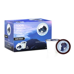 Pode incluir: Uma caixa de 12 cápsulas de café de dose única etiquetadas "100% Jamaica Blue Mountain Coffee Dark Roast" com uma cena de montanha azul e branca na frente. As cápsulas são brancas com um rótulo marrom que diz "Mamae Blue Estate" e uma cena de montanha azul.