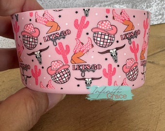 May include: Pink tumbler with a repeating pattern of cowboy hats, cacti, disco balls, and the words "Let's Go Girls".