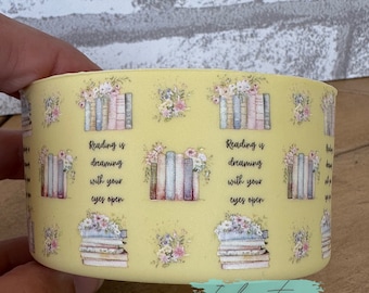 May include: A yellow cylindrical container with a repeating pattern of stacks of books, floral bouquets, and the text "Reading is dreaming with your eyes open".