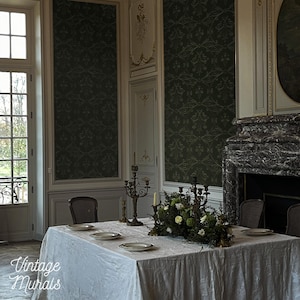 Può includere: Elegante sala da pranzo con un lungo tavolo apparecchiato per un pasto. Il tavolo è coperto da una tovaglia bianca e apparecchiato con piatti, candele e un centrotavola floreale. Le pareti sono decorate con carta da parati verde scuro e modanature.