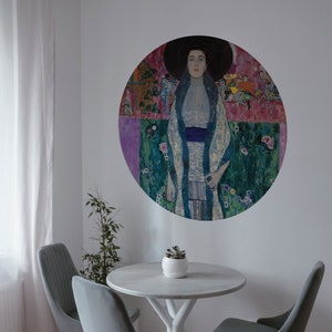 Puede incluir: Un mural de pared redondo con un retrato de una mujer con un sombrero grande, encima de una pequeña mesa redonda y tres sillas grises. La mesa tiene una base blanca y una pequeña maceta blanca con una planta. Las sillas tienen patas blancas.