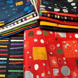 May include: A collection of folded fabric pieces with various colorful patterns. The fabrics feature designs with squares, circles, and lines in shades of blue, red, black, yellow, and green. The fabrics are stacked and arranged together.