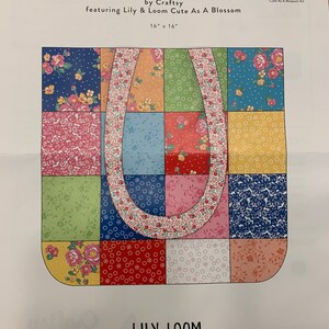 May include: Charm bag craft kit featuring a floral pattern with a blue, green, red, pink, and yellow color scheme. The kit includes fabric pieces to create a 16-inch by 16-inch bag. The kit is titled "Charm Bag Cute As A Blossom Kit" and features the brand "Lily & Loom".