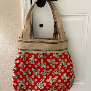 May include: A red and white tote bag with a pattern of bunnies wearing hats. The bag has a brown burlap handle and trim.
