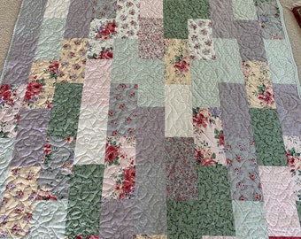May include: A patchwork quilt with a floral pattern in shades of pink, green, and purple. The quilt is quilted with a swirling pattern.