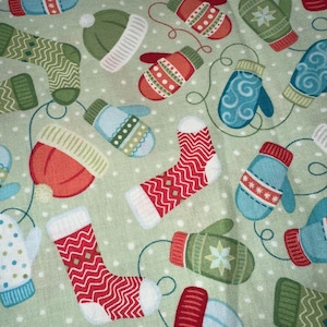 May include: A light green fabric with a repeating pattern of winter hats, mittens, and socks. The mittens and socks have red and white zig-zag patterns. The hats and mittens are in shades of red, green, and blue, with white accents and a dotted background.