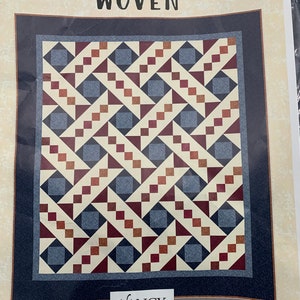 May include: Quilt pattern titled "Woven" featuring a geometric design with red, blue, and brown squares and triangles on a white background. The pattern is framed by a dark blue border. The pattern is by Nancy Rink Designs.