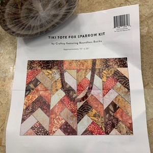 May include: Tiki Tote Fox Sparrow Kit by Craftsy featuring Boundless Batiks. The kit includes fabric for a tote bag with a chevron pattern in shades of brown, orange, and red. The bag is approximately 15 inches by 20 inches.