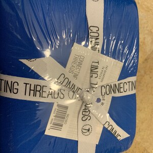 May include: A package of 14 fat quarters of blue fabric with the text "Connecting Threads" on the label. The fabric is wrapped in white ribbon with a small logo of a needle and thread.