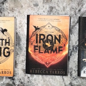 May include: Three paperback books with black and white illustrations on the covers. The books are titled "Fourth Wing", "Iron Flame", and "Onyx Storm". All three books are by Rebecca Yarros.