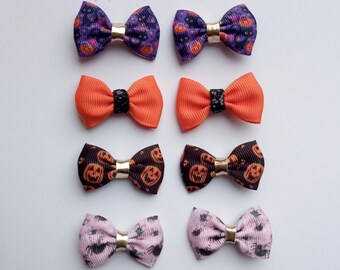 May include: Eight Halloween-themed hair bows in various patterns and colors. The bows include purple with pumpkins, orange with black centers, brown with jack-o'-lanterns, and pink with spiders. Each bow is 1.5 inches and has a gold-colored center.
