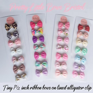 May include: A set of 20 tiny 1 1/2 inch ribbon bows on lined alligator clips. The bows are in a variety of colors and patterns, including pink, purple, blue, green, and white. The bows are arranged in rows on a white background. The text "Handmade with Love" is printed on the cards.