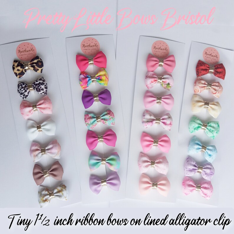 May include: A set of 20 tiny 1 1/2 inch ribbon bows on lined alligator clips. The bows are in a variety of colors and patterns, including pink, purple, blue, green, and white. The bows are arranged in rows on a white background. The text "Handmade with Love" is printed on the cards.