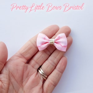 May include: A small pink bow with a white marble pattern and a gold center. The bow is held in a hand.
