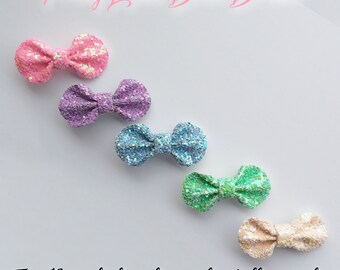 May include: Five glitter bows in pink, purple, blue, green, and beige. Each bow is 1.75 inches wide and attached to a lined alligator clip. The text at the top says "Pretty Little Bows Bristol" and the text at the bottom says "Tiny 1 3/4 inch glitter bows on lined alligator clips."