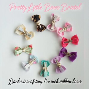 May include: Back view of ten 1 1/2 inch ribbon bows with alligator clips. The bows are in various colors and patterns, including floral, leopard print, and solid colors.