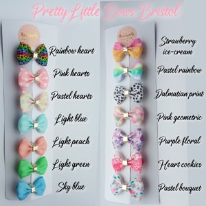 May include: A set of 10 handmade hair bows with various patterns and colors, including rainbow hearts, pink hearts, pastel hearts, light blue, light peach, light green, sky blue, strawberry ice-cream, pastel rainbow, dalmatian print, pink geometric, purple floral, heart cookies, and pastel bouquet.