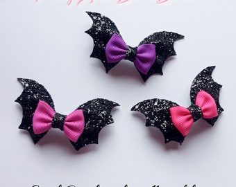May include: Three bat-shaped hair clips with glittery black wings and colorful bows. The bows are in pink and purple. The text "Pretty Little Bows Bristol" and "3 inch Bat clip with tiny 1 1/2 inch bow" are visible.