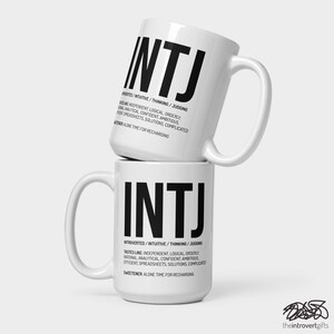 May include: White ceramic mug with a black graphic of the letters INTJ and a definition of the Myers-Briggs personality type. The mug is stacked on top of another identical mug.