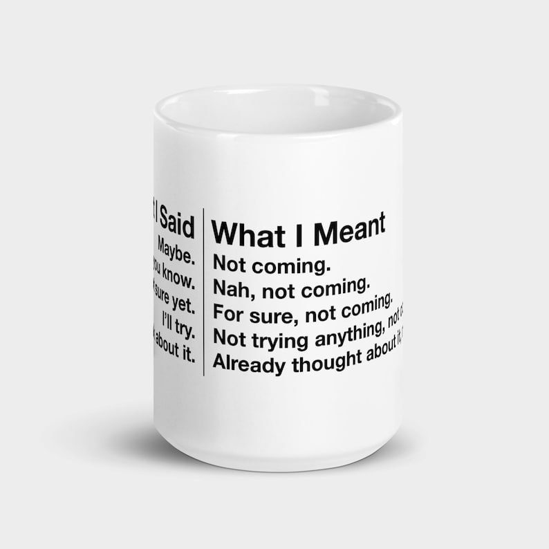 May include: A white ceramic mug with black text. The text on the mug reads "What I Said" on the left side and "What I Meant" on the right side. The mug is cylindrical and has a handle.