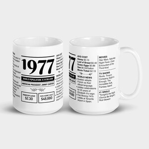 Op de afbeelding: Twee witte keramische mokken met zwarte tekst. Eén mok toont het jaar "1977" met informatie zoals de wereldbevolking, de Amerikaanse president en de gemiddelde huizenprijs. De andere mok bevat vergelijkbare informatie, inclusief film- en tv-titels.