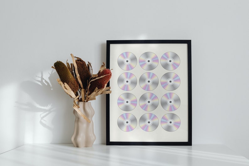 K&ouml;nnte beinhalten: Ein gerahmter Druck eines minimalistischen Designs mit zw&ouml;lf silbernen CDs, die in einem Raster angeordnet sind. Die CDs haben einen regenbogenfarbenen, irisierenden Glanz.