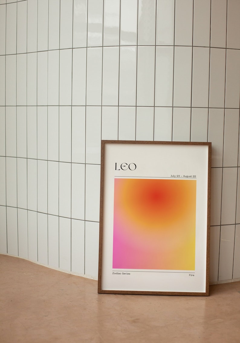 May include: A framed print with a gradient background in shades of pink, orange, and yellow. The print features the text "Leo" and "Zodiac Series" in black text. The text "July 23 - August 22" and "Fire" are also included in black text.