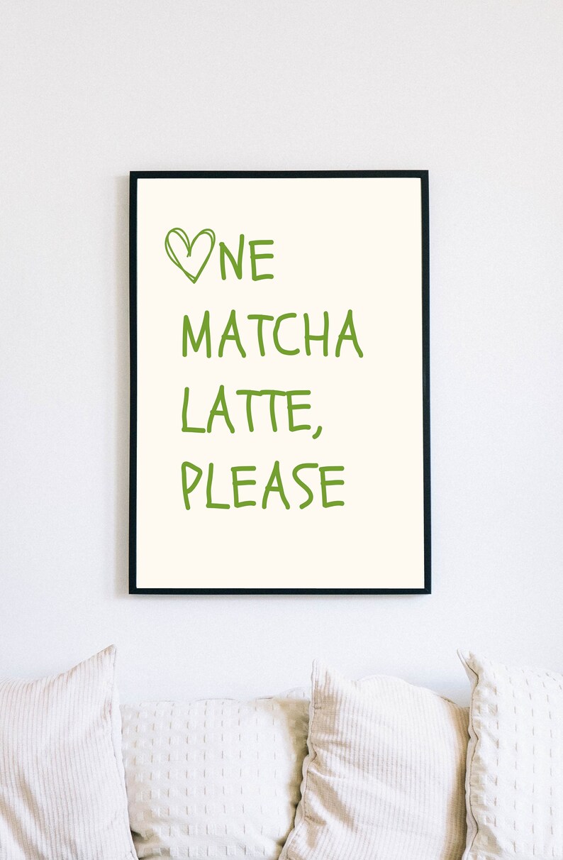 May include: A framed print featuring the text "One Matcha Latte, Please" in green, handwritten lettering. The words are set against a cream backdrop, with a green heart above "One". The frame is black.