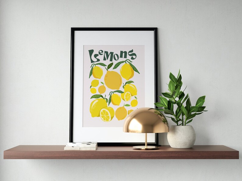 May include: A framed print with a light pink background and the text "Les Mons" in green. The print features a cluster of yellow lemons with green leaves.