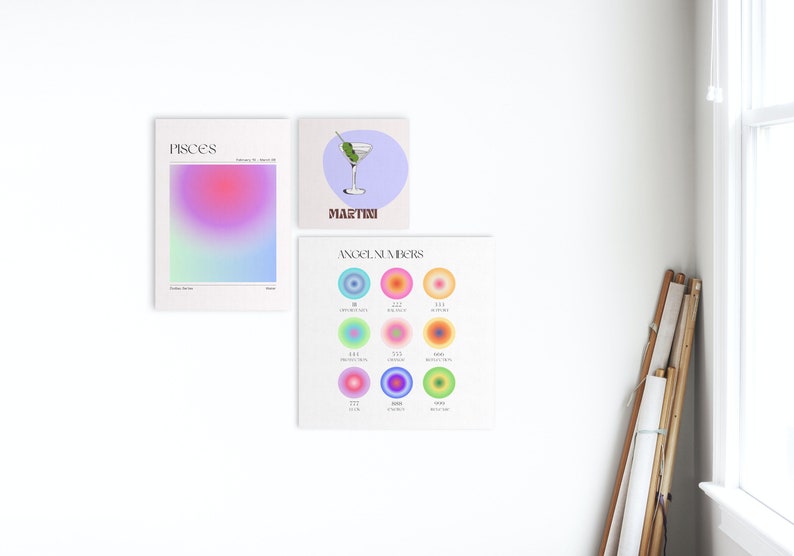 May include: Three colorful prints on a white wall. The first print is a gradient of pink, blue, and green with the word "Pisces" at the top. The second print is a light blue background with a martini glass and the word "Martini" at the bottom. The third print is a light green background with the words "Angel Numbers" at the top and nine colorful circles with numbers inside.