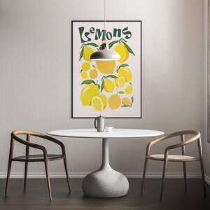 May include: A white table with a light wood chair on each side. A black framed poster with the word "Lemons" in green text and a yellow lemon illustration is hanging on the wall behind the table. A light fixture hangs above the table.