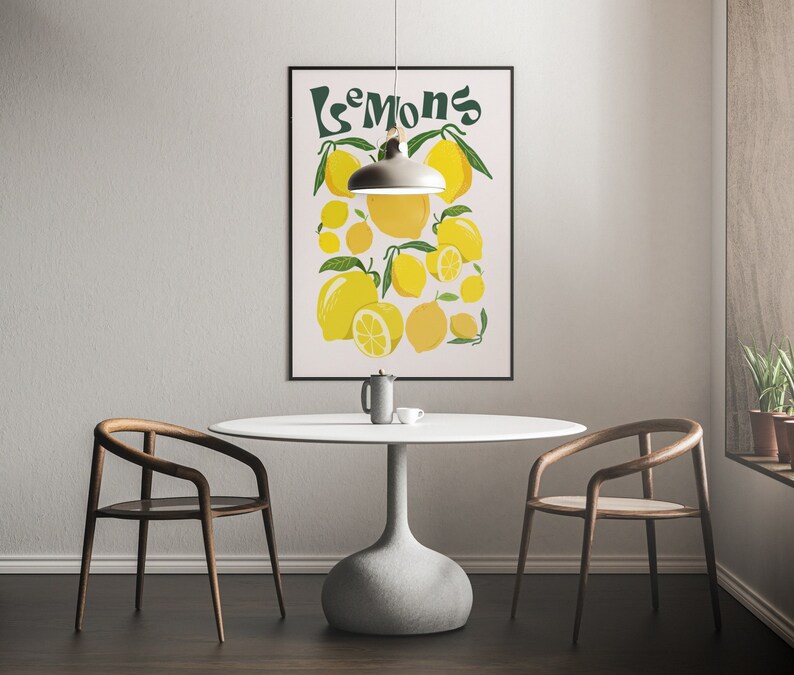 May include: A white table with a light wood chair on each side. A black framed poster with the word "Lemons" in green text and a yellow lemon illustration is hanging on the wall behind the table. A light fixture hangs above the table.