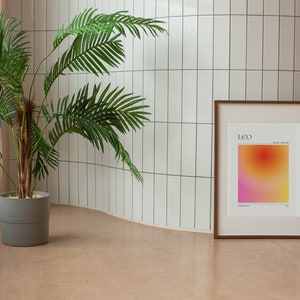 May include: A framed print with a gradient background in shades of pink, orange, and yellow. The print has the word "LEO" in black text at the top and the dates "July 23 - August 22" in smaller black text below. The frame is brown wood.